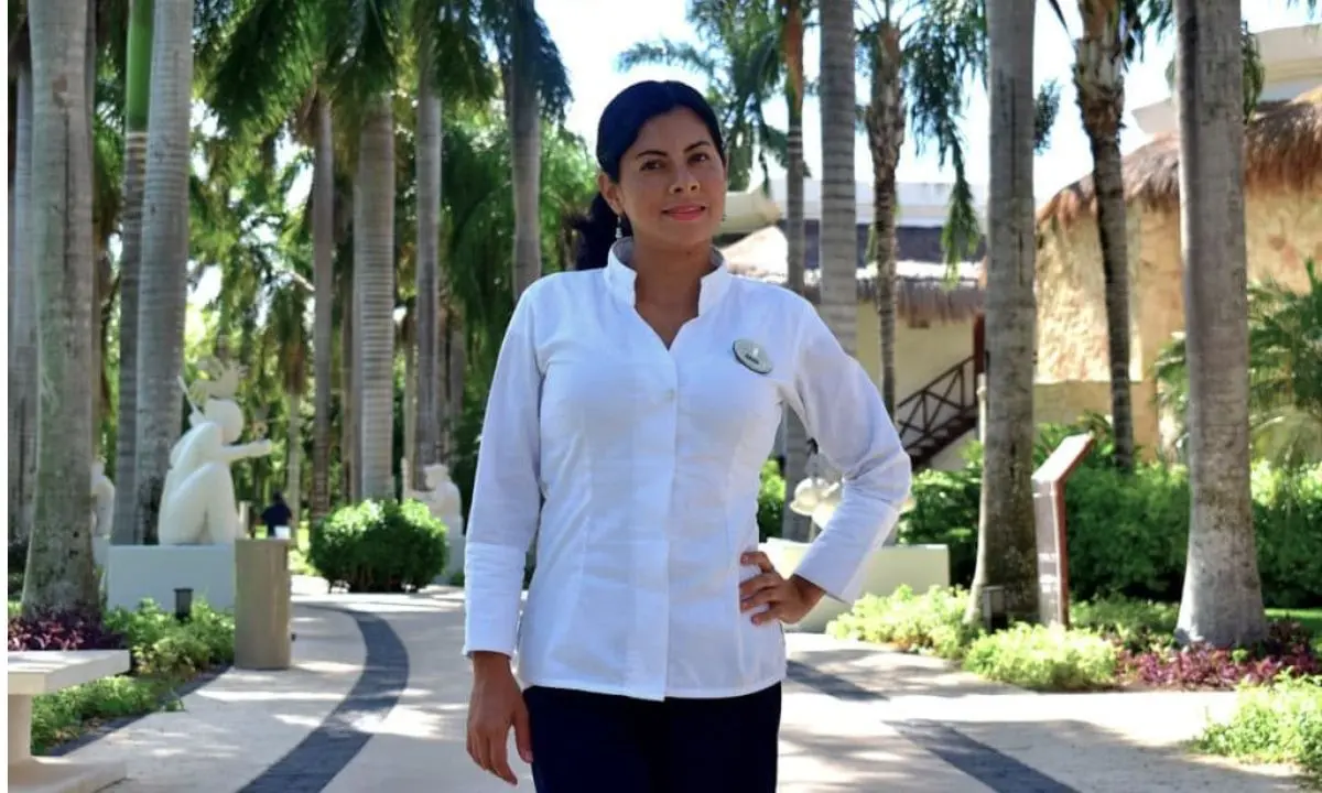 Mujer uniformada con gorro azul en un camino entre palmeras.