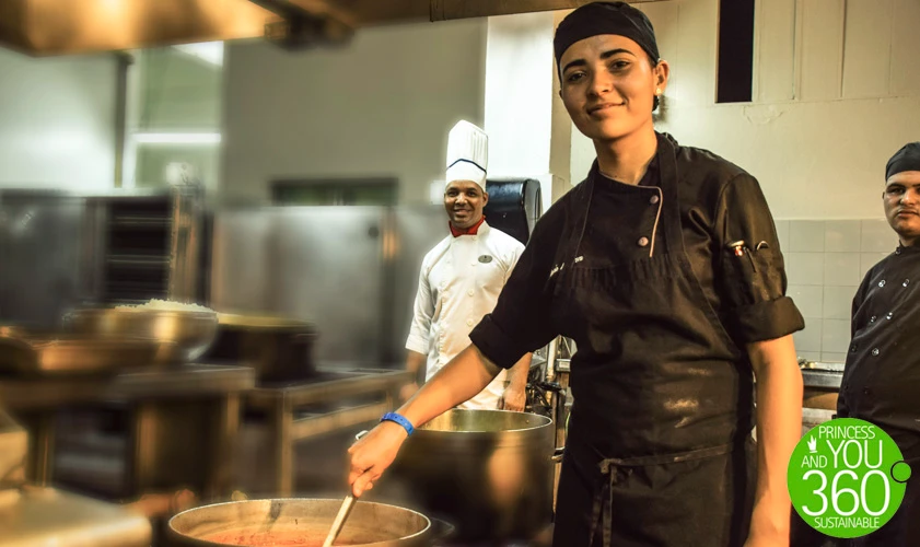 Cocinera con gorro y uniforme negro prepara comida en cocina profesional.