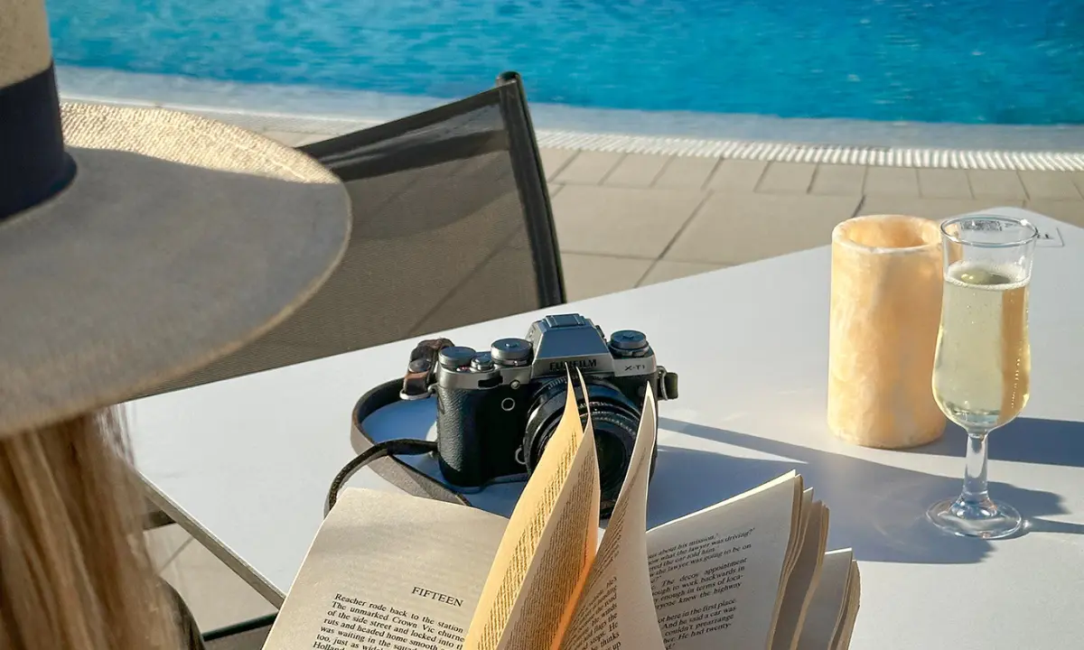 C&aacute;mara profesional sobre mesa con dos bebidas junto a piscina al sol