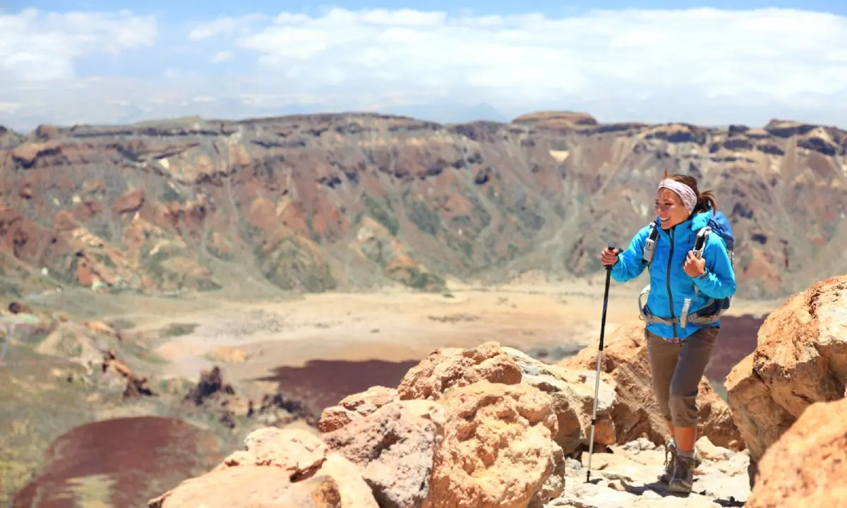 Senderista con mochila y bast&oacute;n en rocas, en un paisaje monta&ntilde;oso.