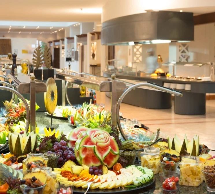 Mesa buffet con frutas frescas, ensaladas y recipientes en un restaurante.