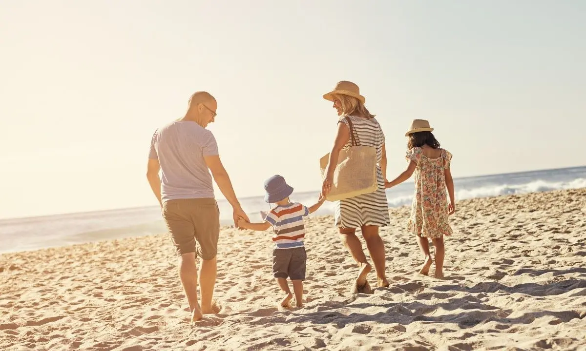 Familia caminando por la playa al atardecer, con sombreros y ni&ntilde;os