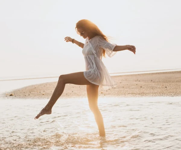 Mujer corriendo descalza en la playa con vestido blanco y luz de sol