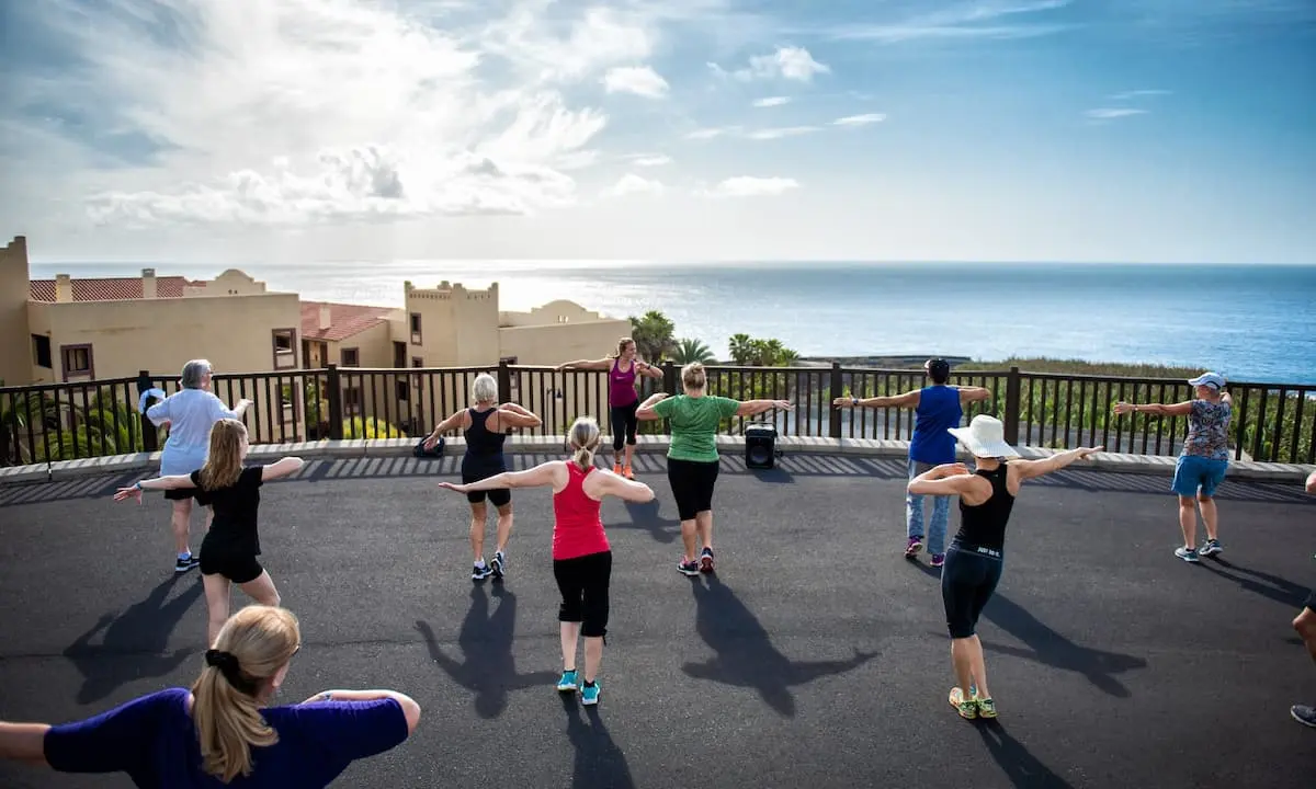 Personas haciendo ejercicios en terraza con vista al mar y cielo nublado