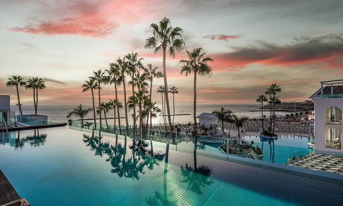 Piscina del hotel con palmeras y el mar al atardecer, cielo rosado