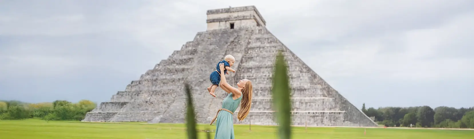 Mujer con beb&eacute; en brazos frente a la pir&aacute;mide maya de Chich&eacute;n Itz&aacute;