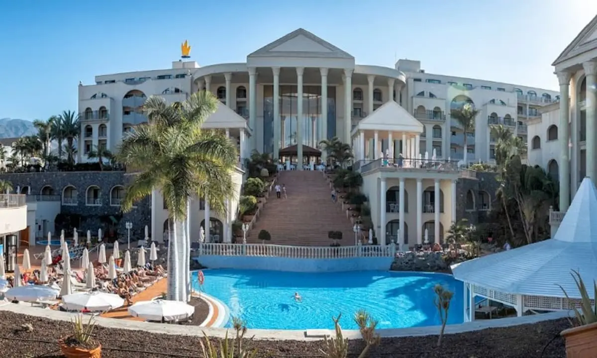 Hotel con piscina azul y palmeras, arquitectura blanca junto al mar