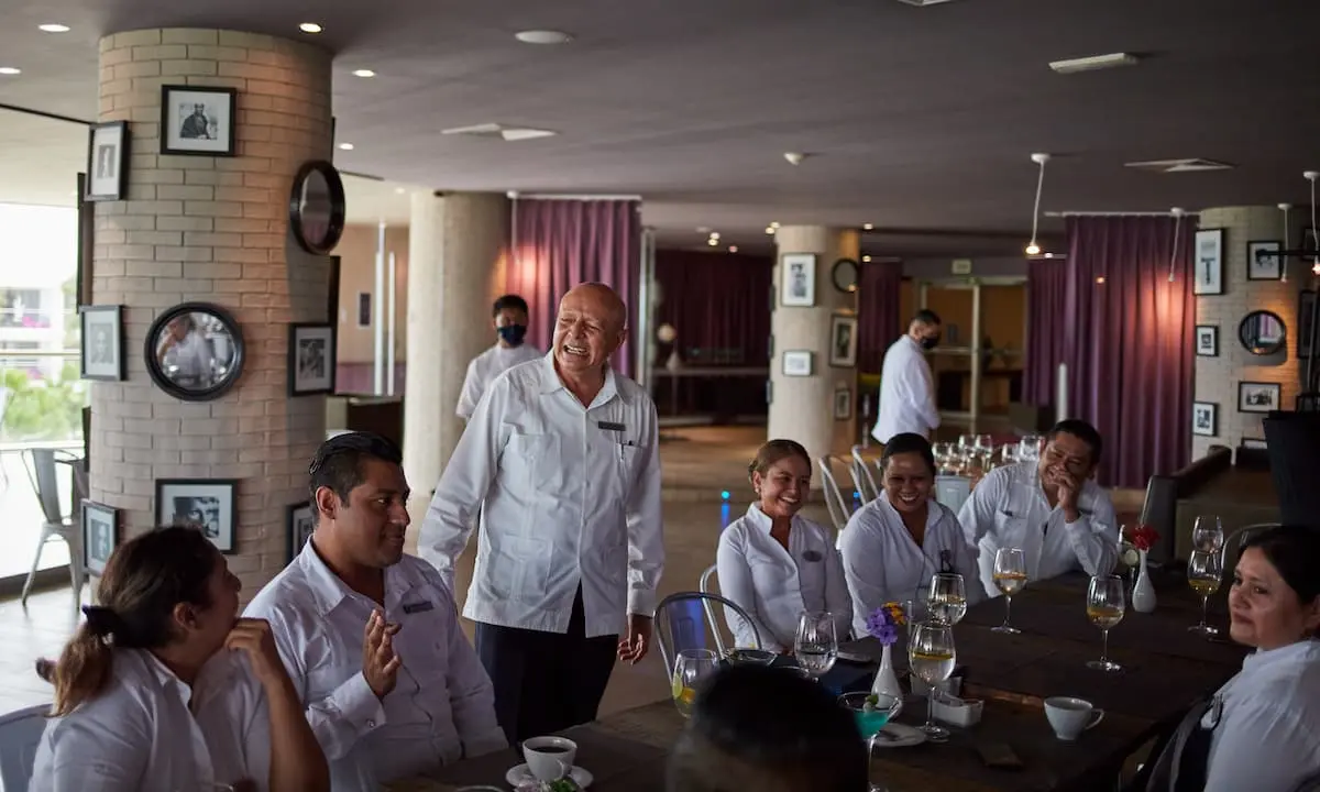 Chef mayor sonriente habla a su equipo en comedor con copas y platos