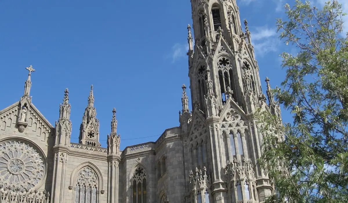 Fachada de una catedral g&oacute;tica de piedra con torres y cielo azul.
