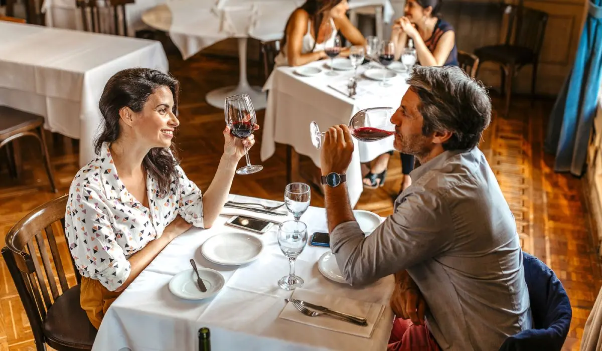 Pareja brinda con copas de vino en una mesa de restaurante, sonrientes