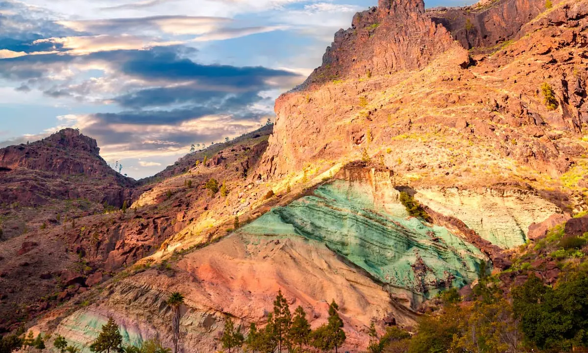 Ca&ntilde;&oacute;n escarpado con r&iacute;o seco y estratos de colores bajo el cielo nublado