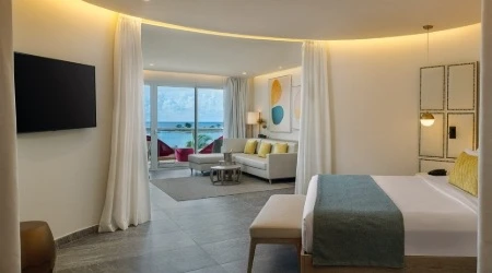 Sala de hotel con cama, sill&oacute;n y cortinas, vista al mar.