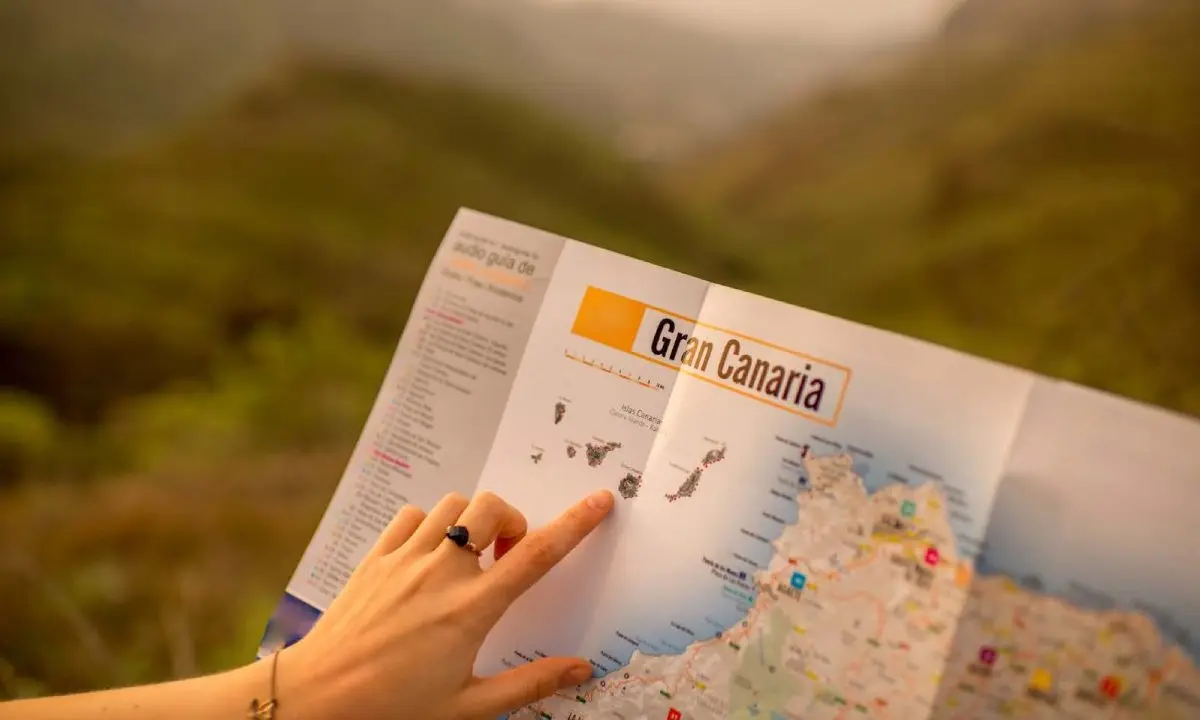 Mano se&ntilde;alando un mapa tur&iacute;stico &ldquo;Gran Canaria&rdquo; sobre fondo borroso.
