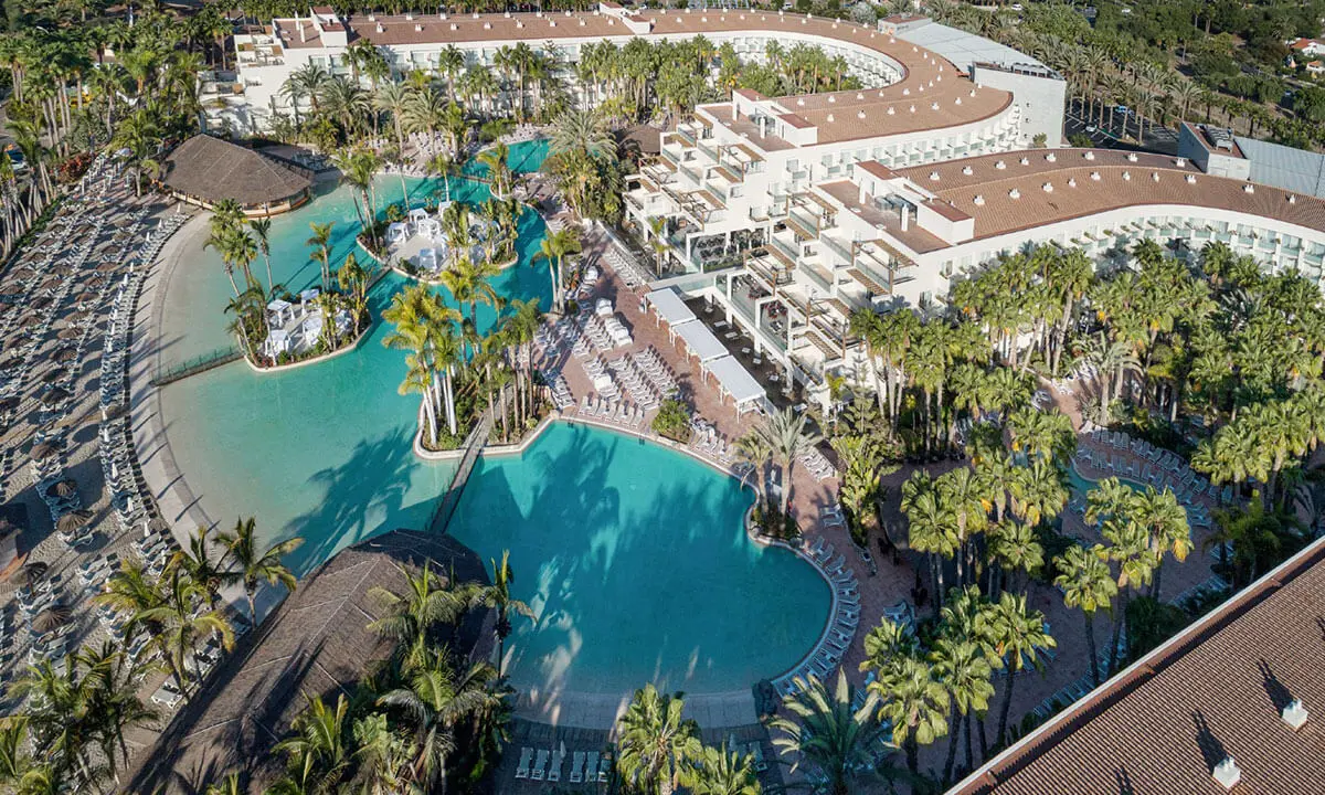 Vista a&eacute;rea de un hotel con piscinas, palmeras y edificios junto al mar