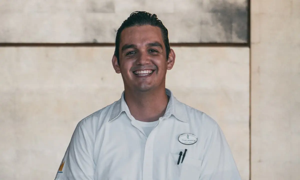 Hombre sonriente con camisa blanca en un interior.