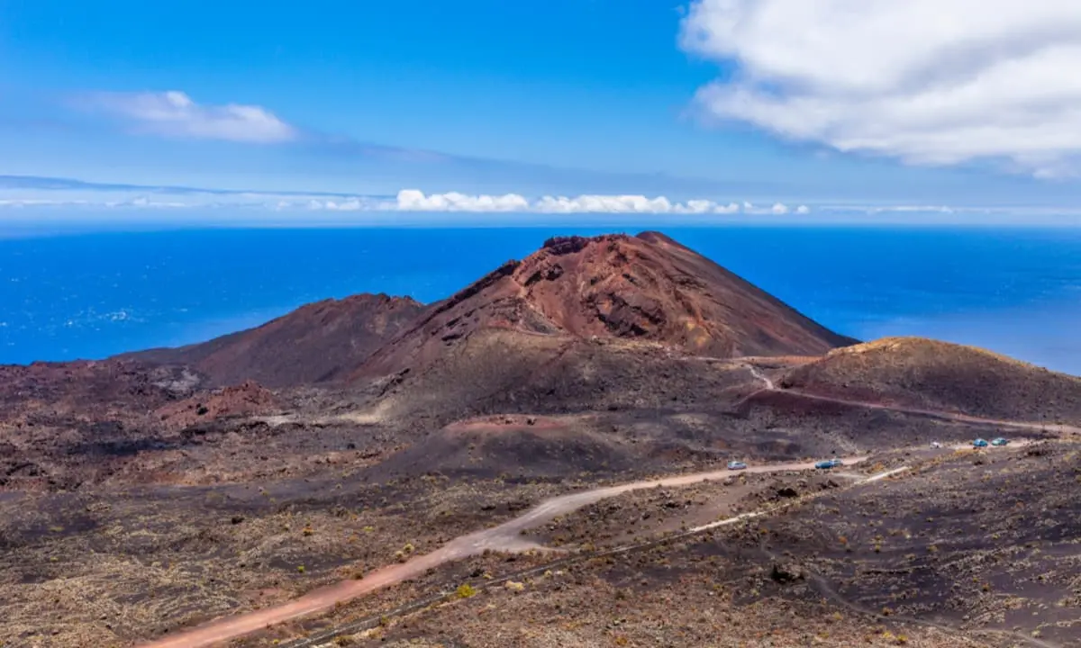 Monta&ntilde;a volc&aacute;nica sobre un paisaje &aacute;rido con carretera y el mar azul al fondo