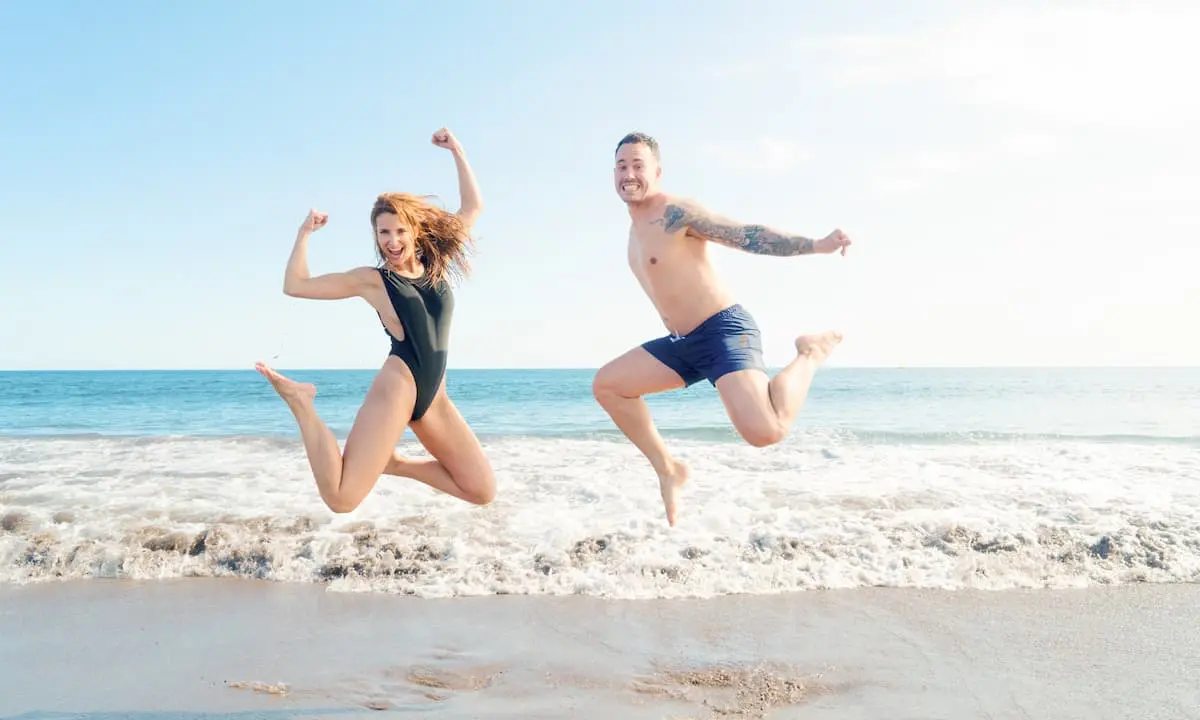Pareja saltando en la playa, con el mar y espuma de fondo