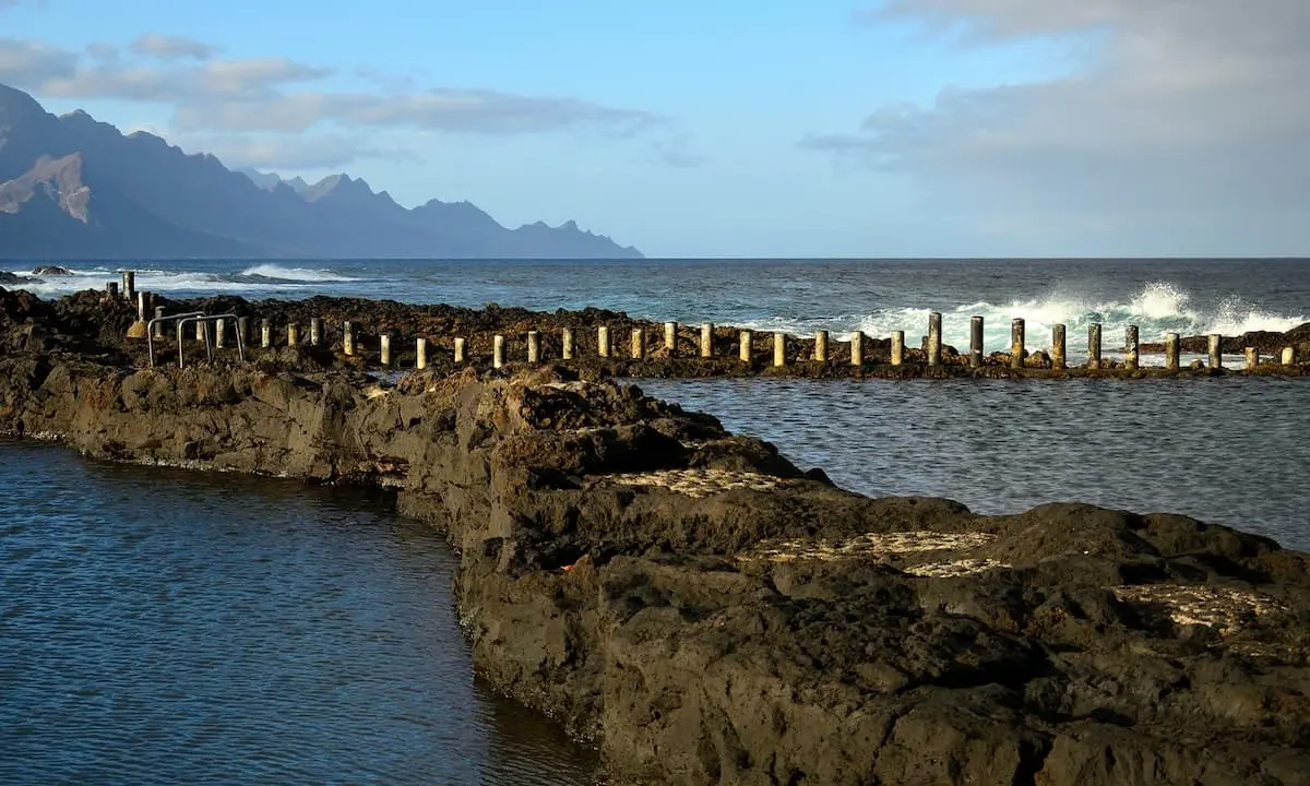Muro de troncos y olas en la costa con monta&ntilde;as al fondo