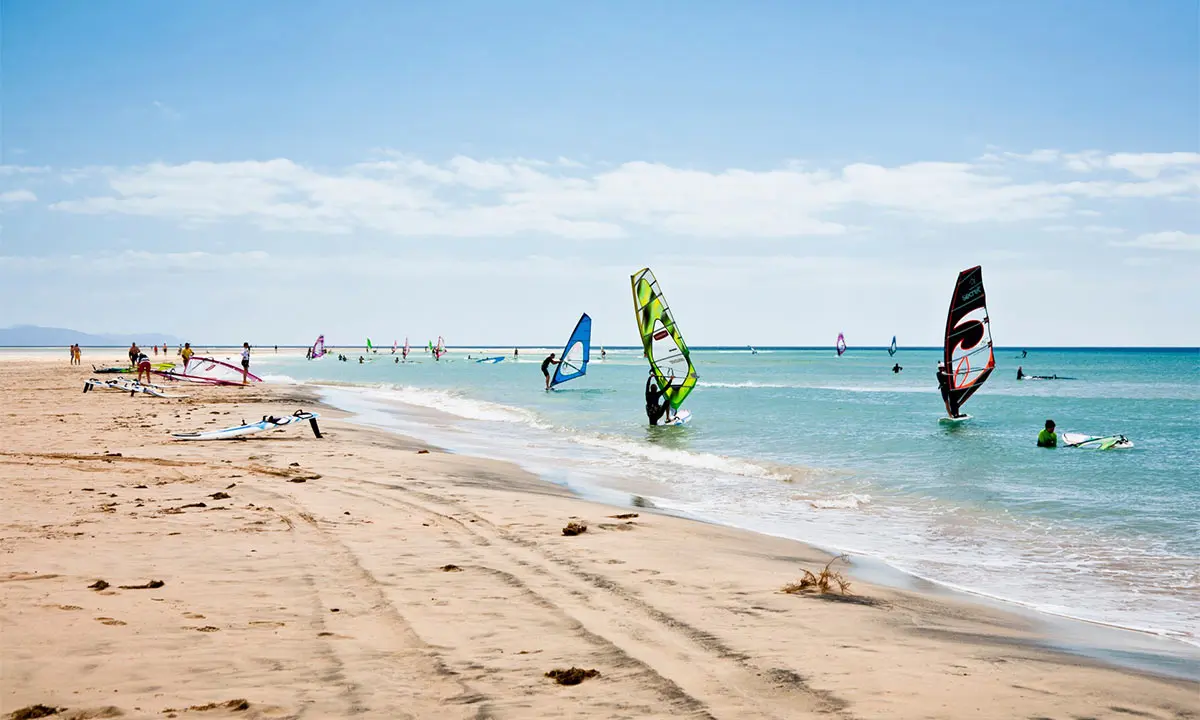 Windsurfistas en la playa con velas y tablas sobre el mar azul