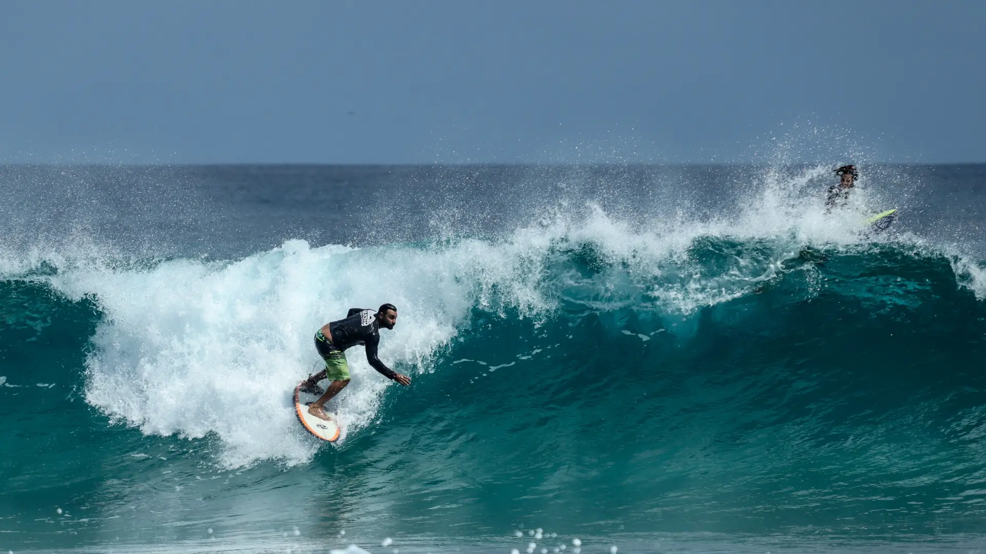 Surfista surfeando una ola grande con tabla naranja, salpicando agua.