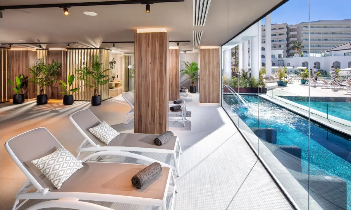 Terraza moderna con camastros, palmeras y piscina climatizada con vistas al mar