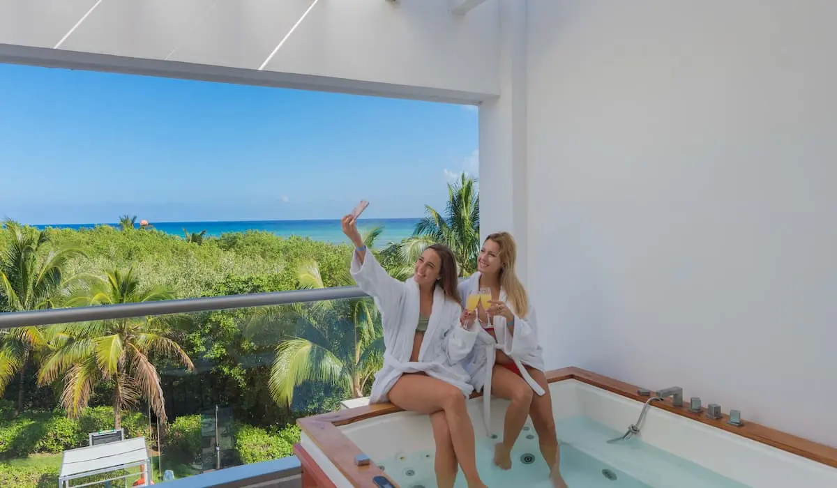 Dos mujeres en jacuzzi con vista al mar y palmeras, dentro de una caba&ntilde;a.