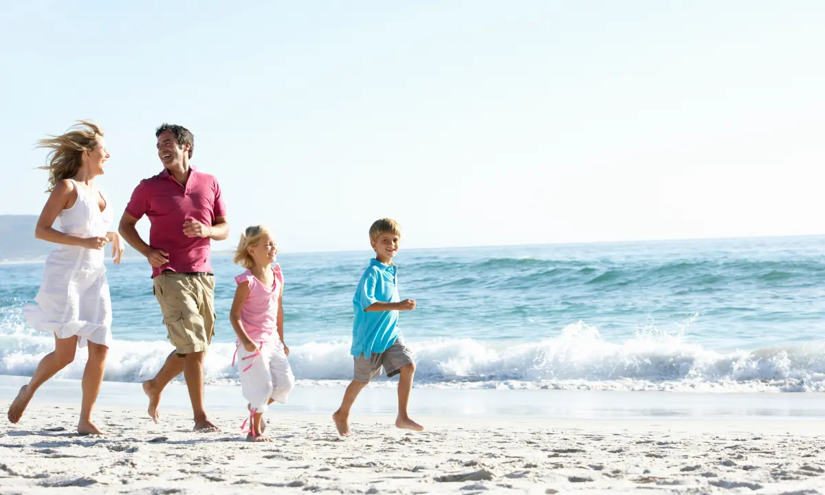 Familia corriendo y riendo en la playa junto al mar, al aire libre.