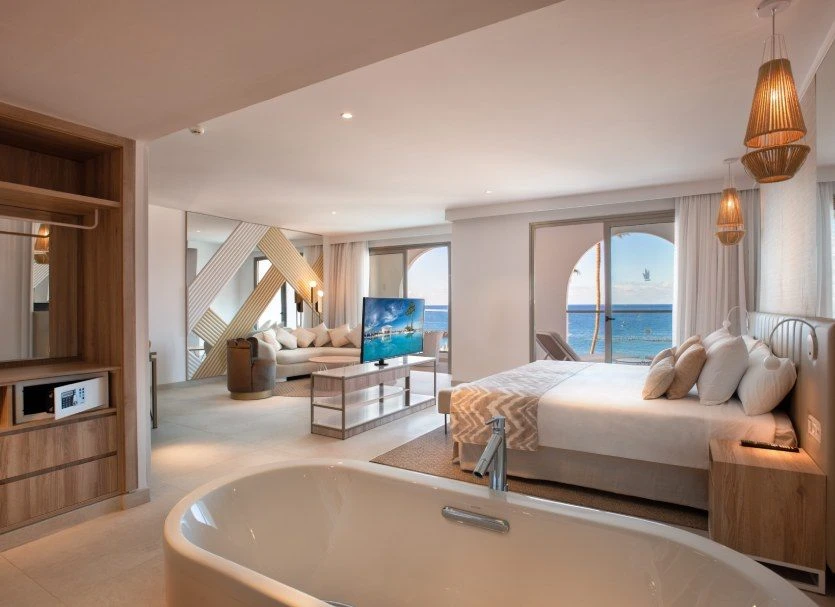Habitaci&oacute;n hotelera con ba&ntilde;era, cama grande, sala y vista al mar.