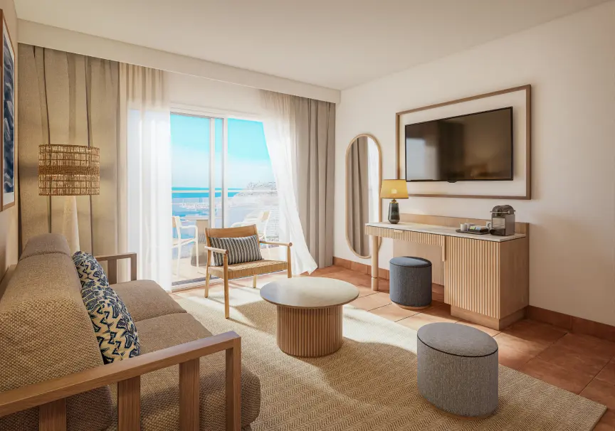 Sala de hotel luminosa con sillones, mesa redonda y acceso a balc&oacute;n al mar