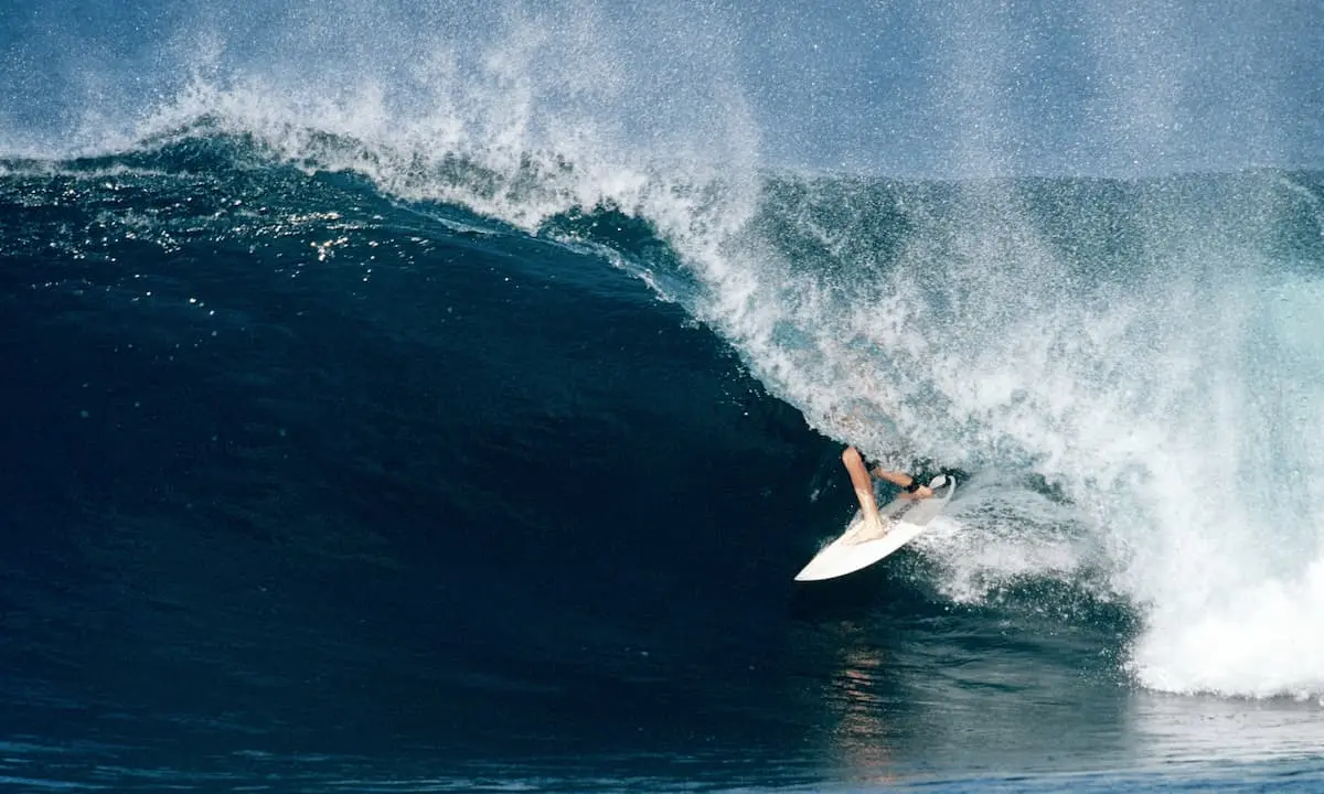Surfista sobre una ola grande y espumosa, salpicando agua desde una tabla blanca