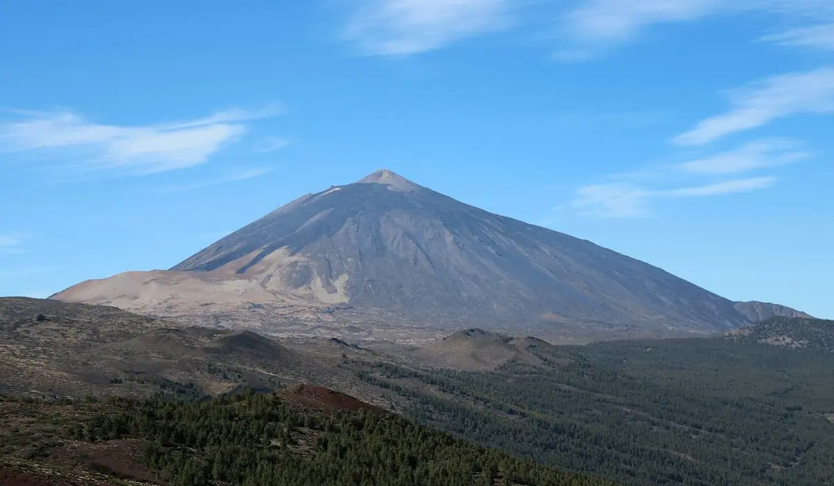 Monta&ntilde;a volc&aacute;nica al fondo bajo cielo azul con nubes.