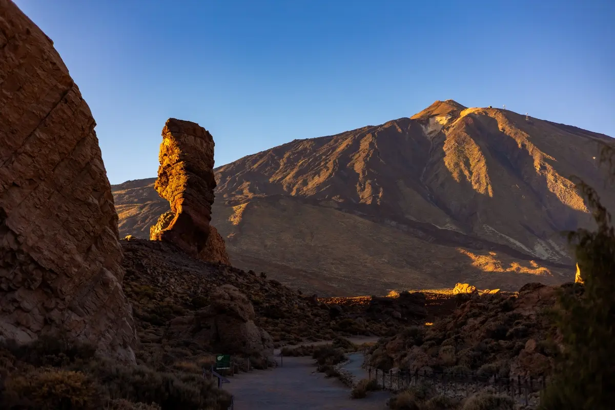 Monta&ntilde;a rocosa al atardecer con sendero entre rocas y luz dorada en la cima