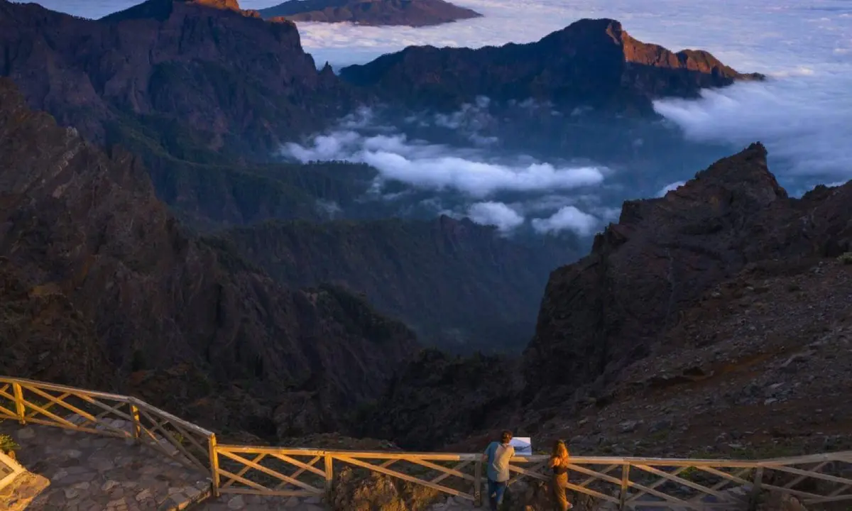 Mirador en monta&ntilde;as con nubes entre valles y dos personas en barandilla