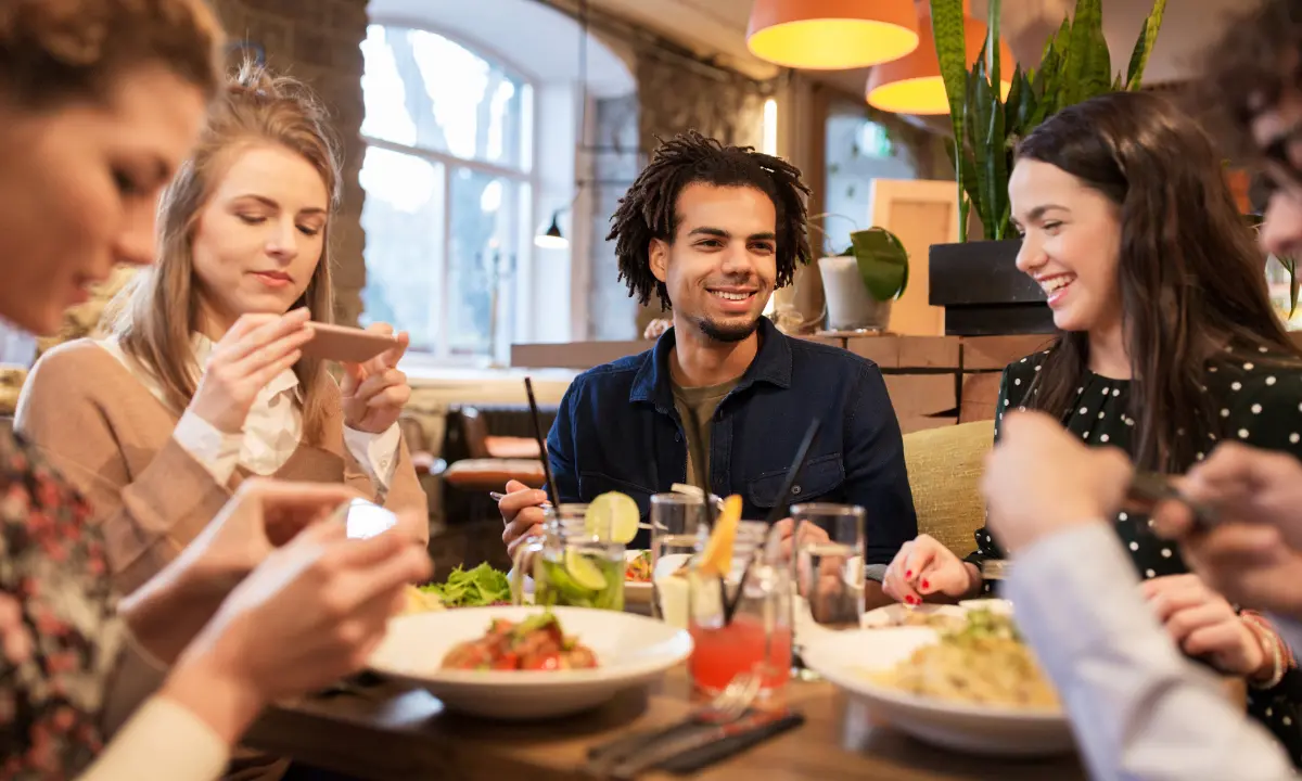 Grupo de amigos sonrientes cenando en un restaurante, con bebidas y platos