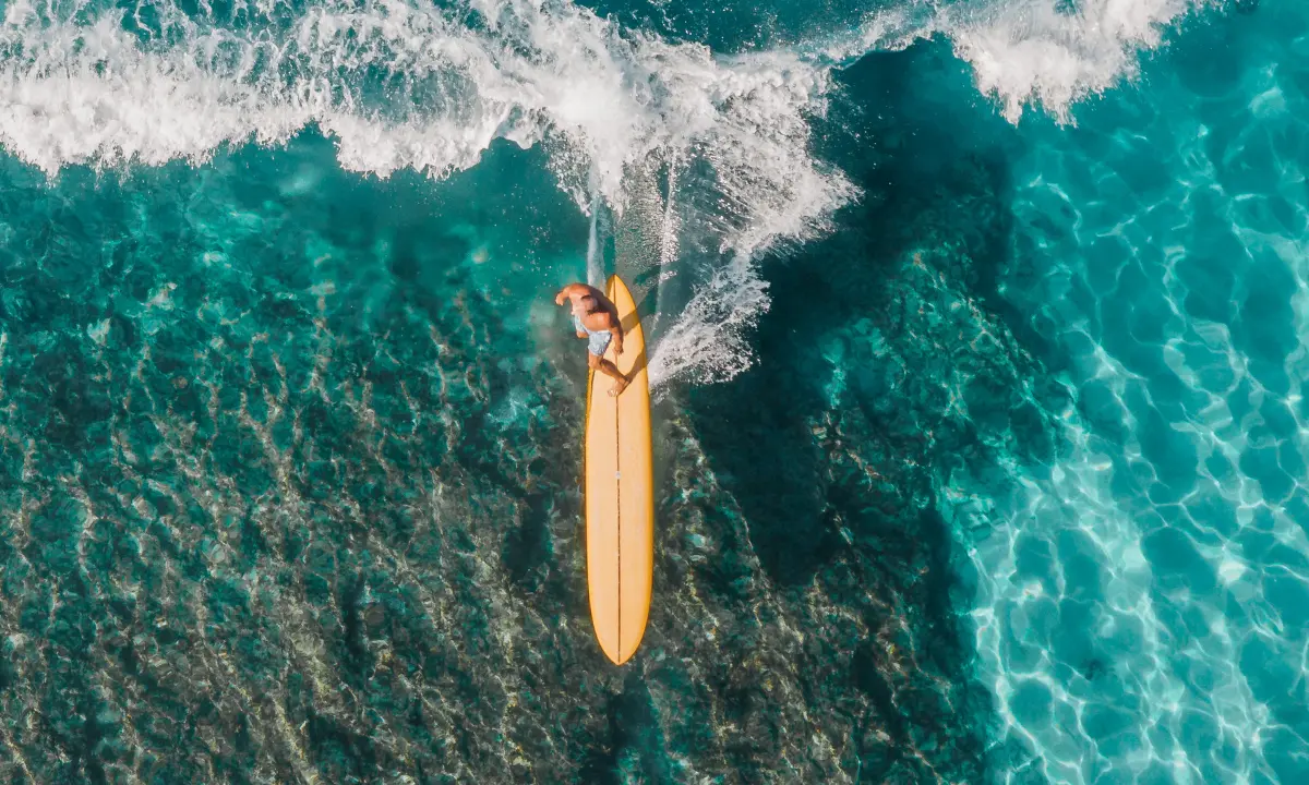 Surfer en tabla amarilla bajo olas sobre aguas turquesa claras