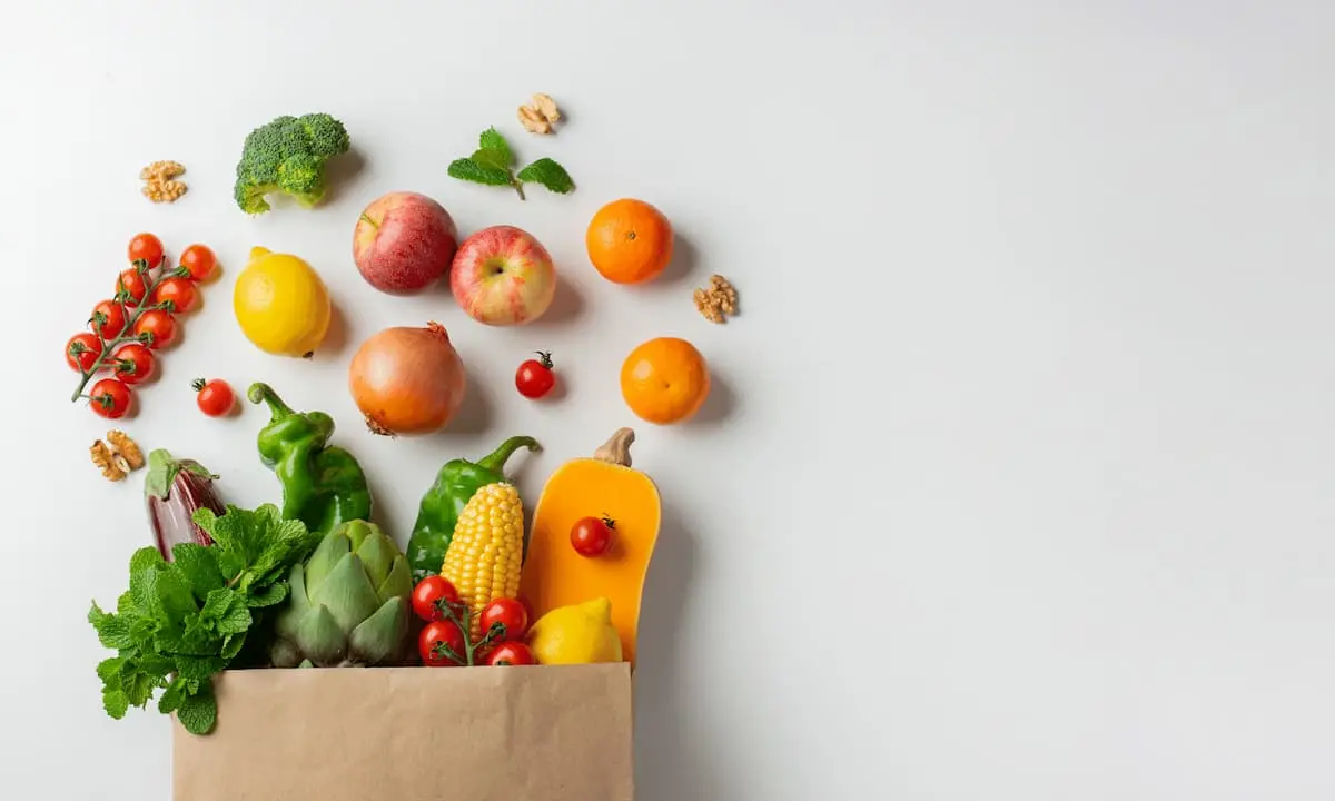 Bolsa de papel con frutas y verduras frescas sobre fondo blanco