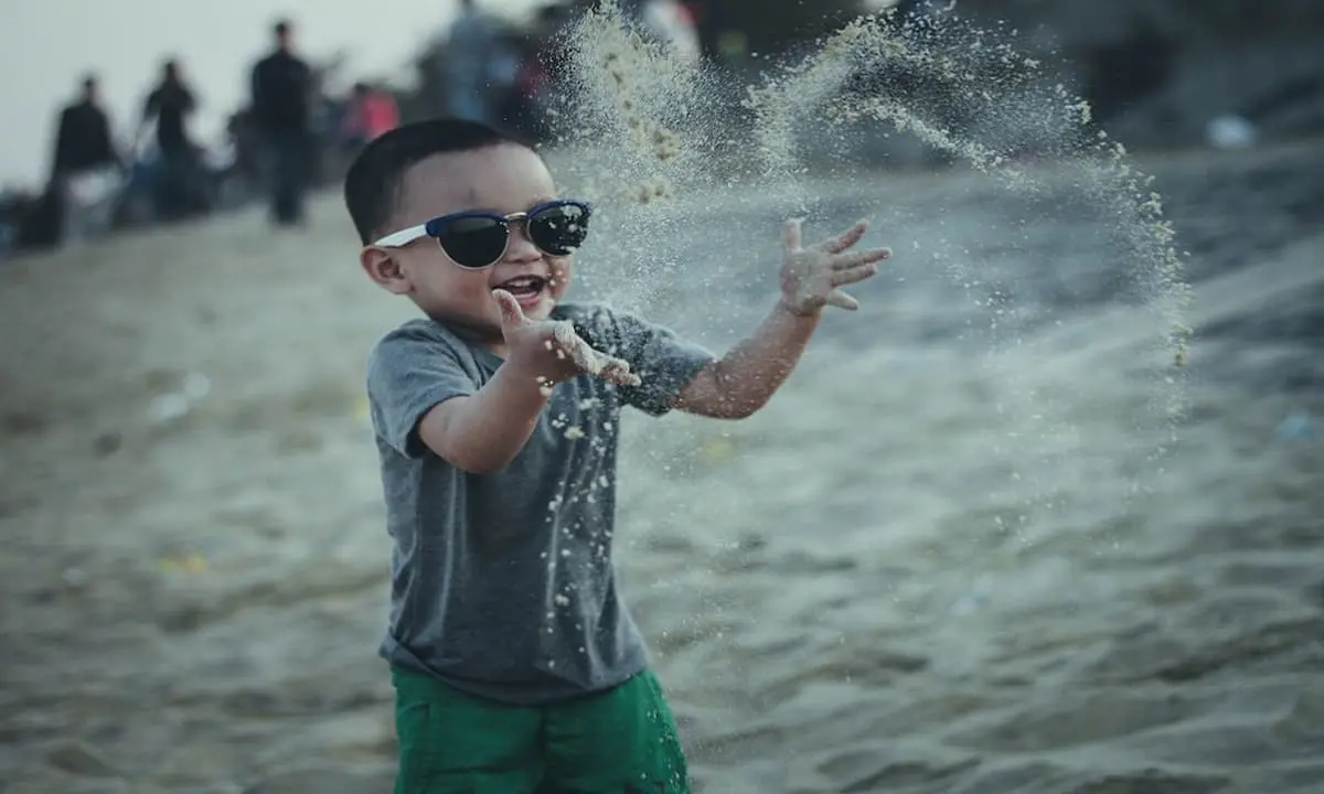 Ni&ntilde;o con gafas de sol juega con agua salpicando en una playa.