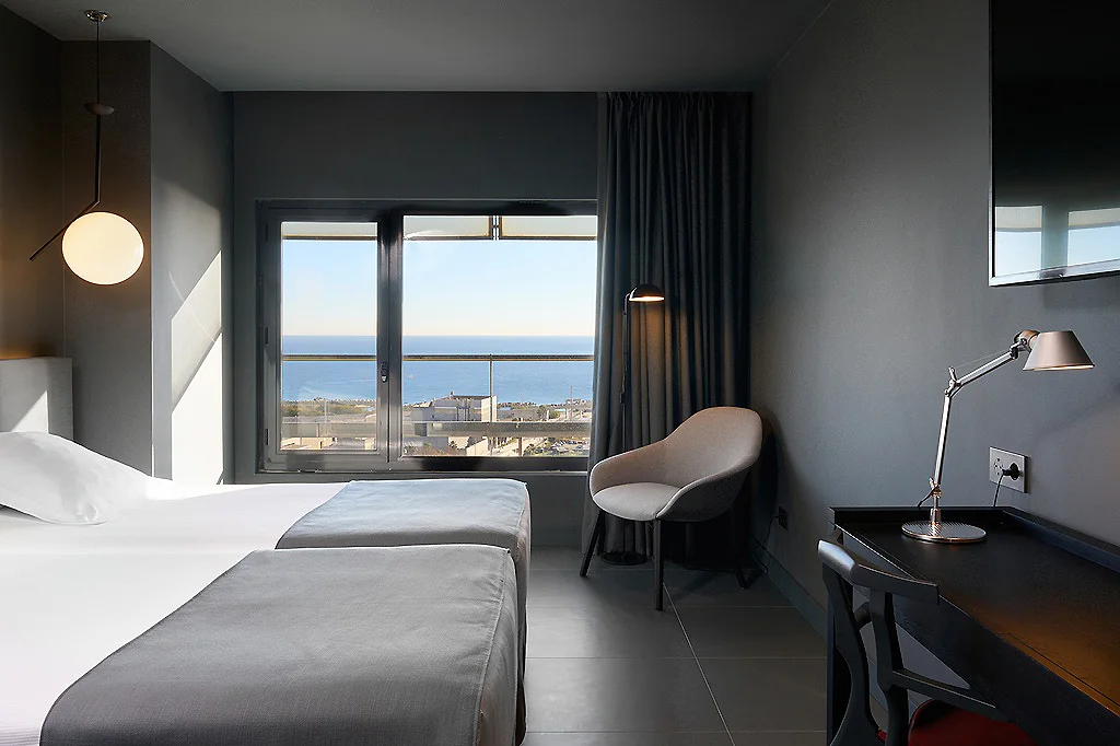 Habitaci&oacute;n hotelera moderna con dos camas y ventana al mar, luz c&aacute;lida