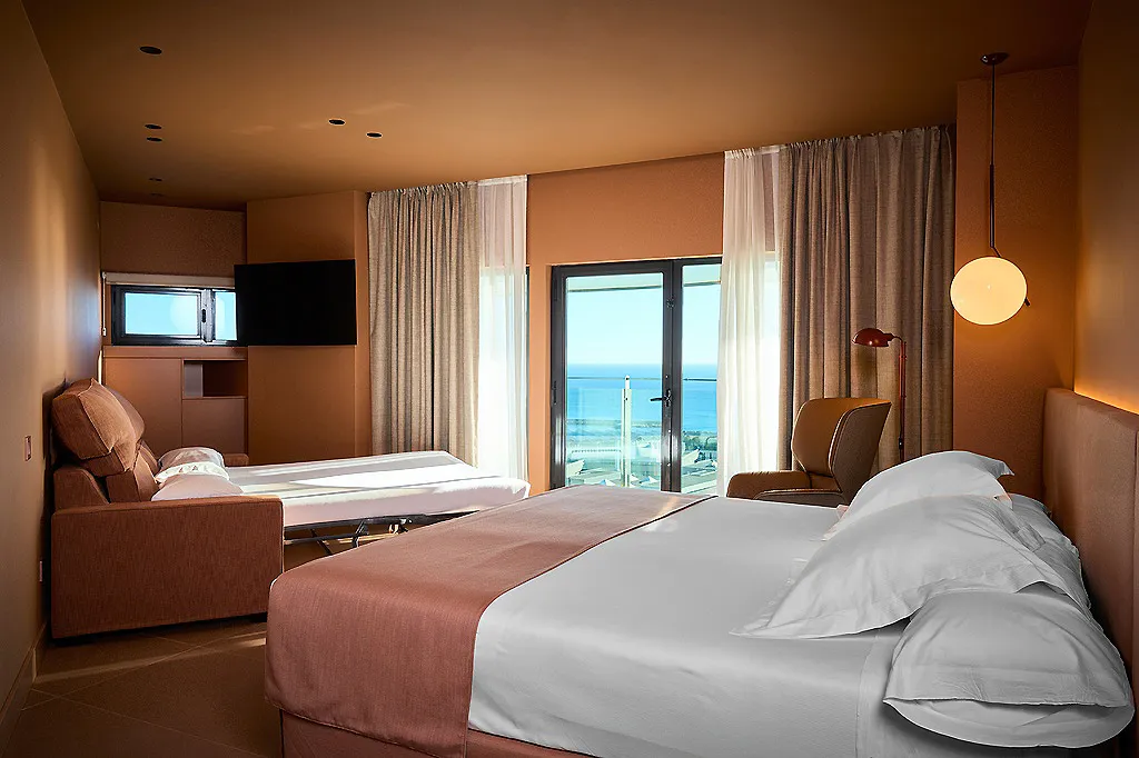 Habitaci&oacute;n de hotel moderna con camas, cortinas y vista al mar