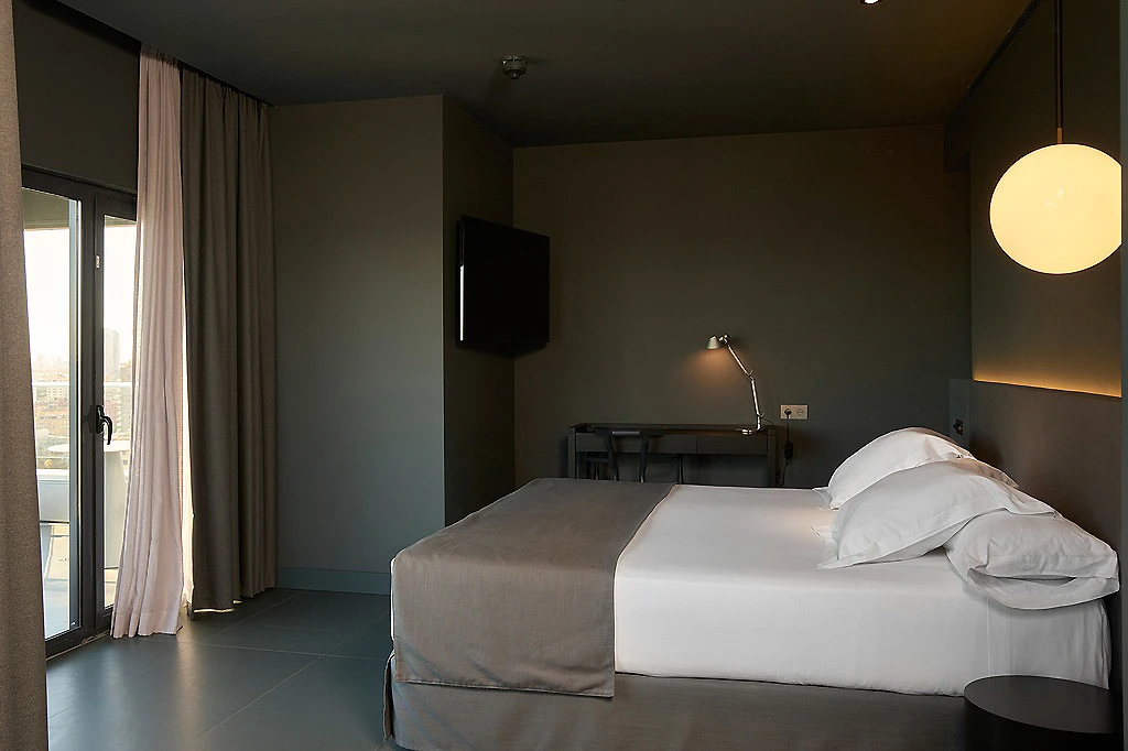 Habitaci&oacute;n de hotel moderna con cama doble y l&aacute;mpara de techo.