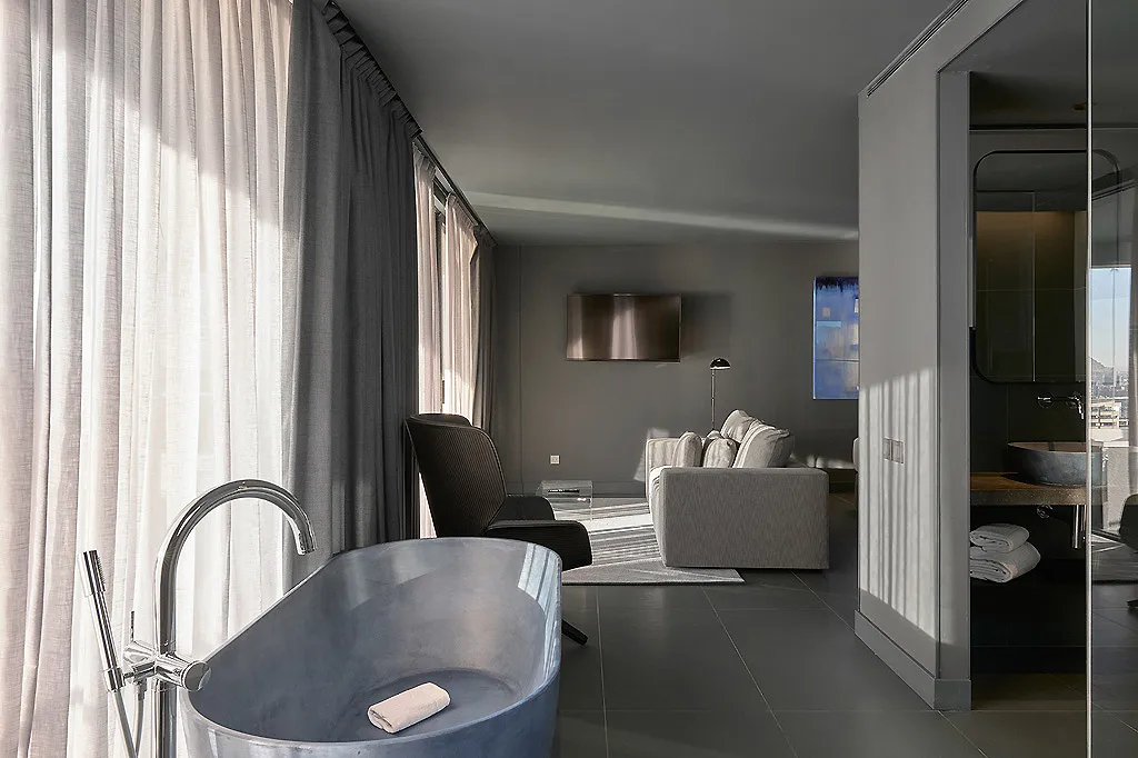 Sala moderna con ba&ntilde;era oval, cortinas grises, sill&oacute;n y puerta de vidrio