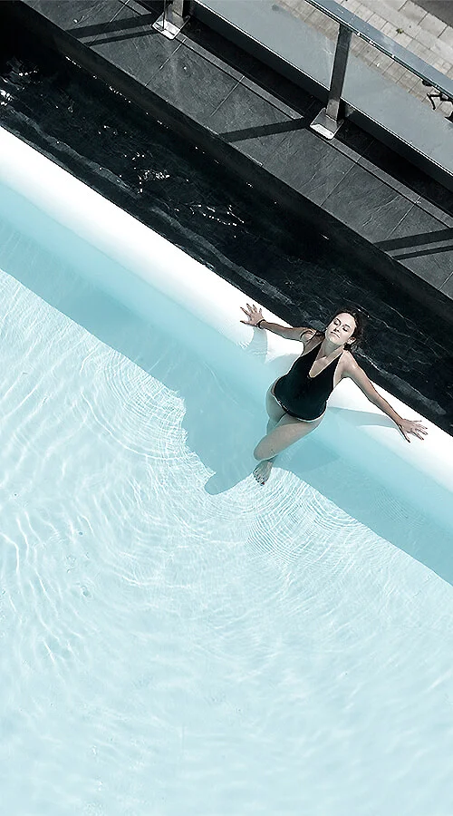 Mujer en pose de nataci&oacute;n, con agua y sombra en una piscina.