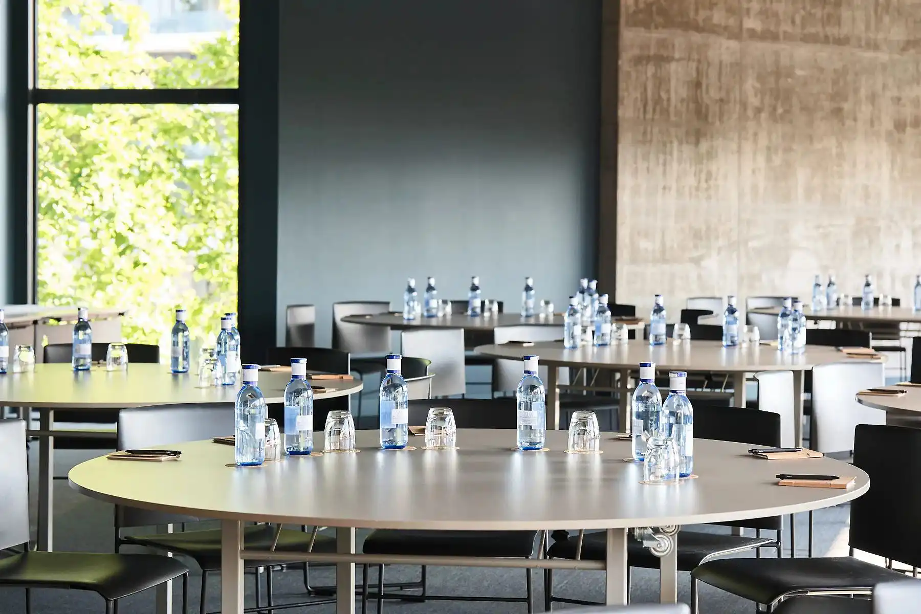 Sala de reuniones con mesa redonda y botellas de agua frente a ventanas