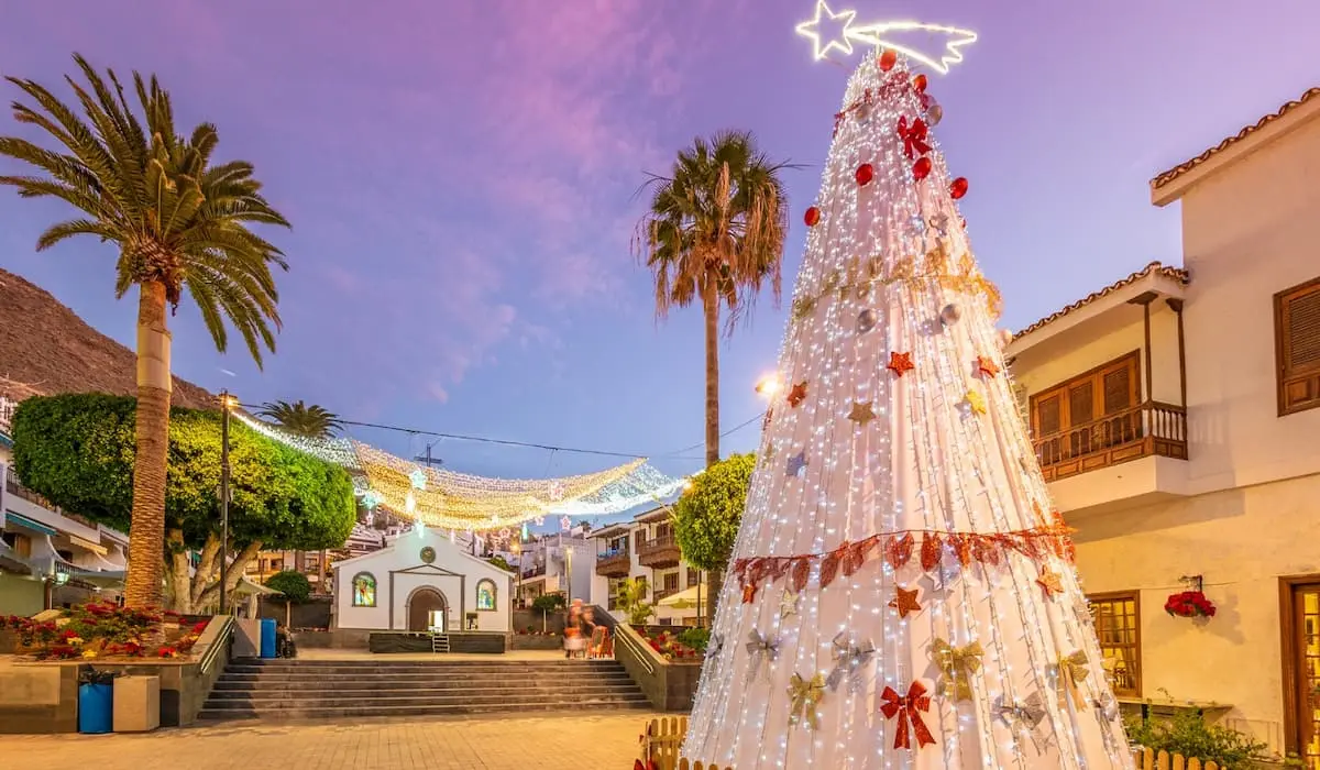 &Aacute;rbol de Navidad luminoso con luces y lazos, en plaza con palmeras.