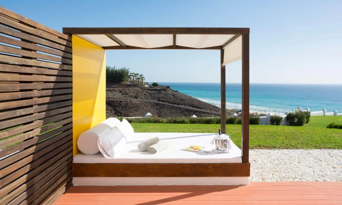 Cama con dosel y vista al mar desde una terraza junto al jard&iacute;n