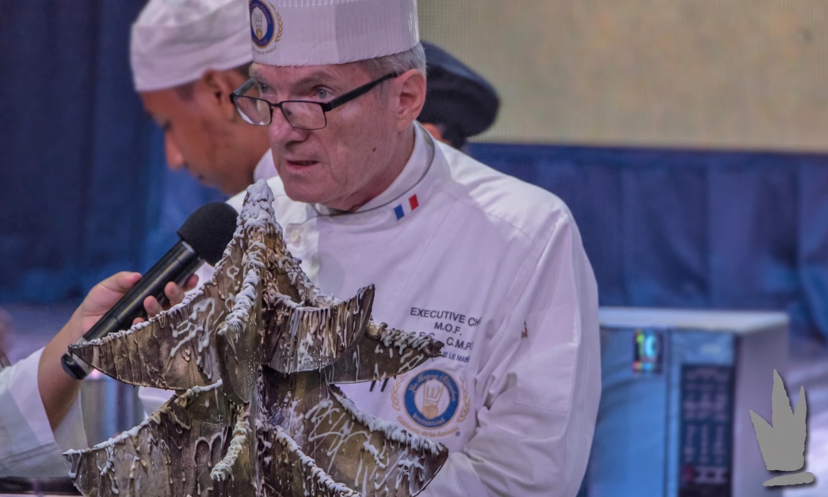 Chef con gorra y uniforme blanco, hablando y se&ntilde;alando un bocadillo.
