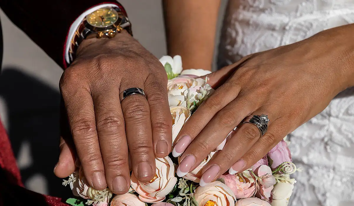 Manos de una pareja con anillos acomodando una boina floral de boda