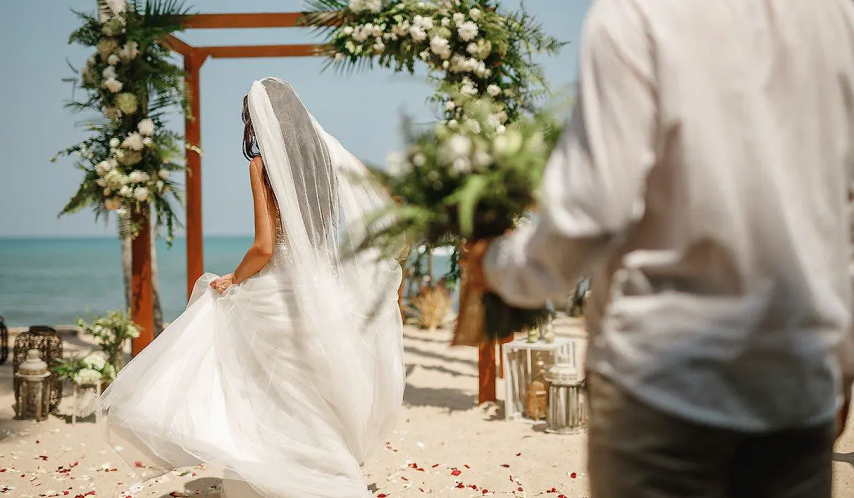 Novia de blanco en una ceremonia junto al mar, con arco floral y velo