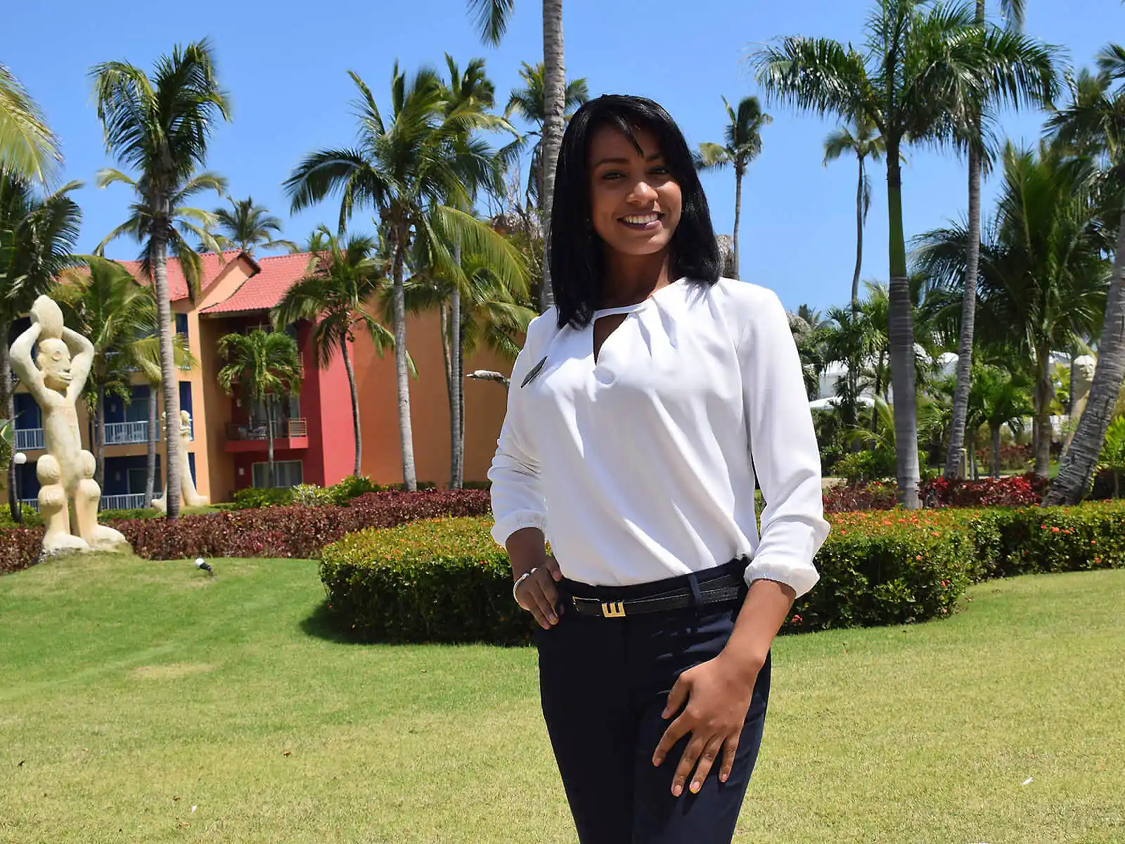 Mujer sonriente con blusa blanca en jard&iacute;n tropical con palmeras.