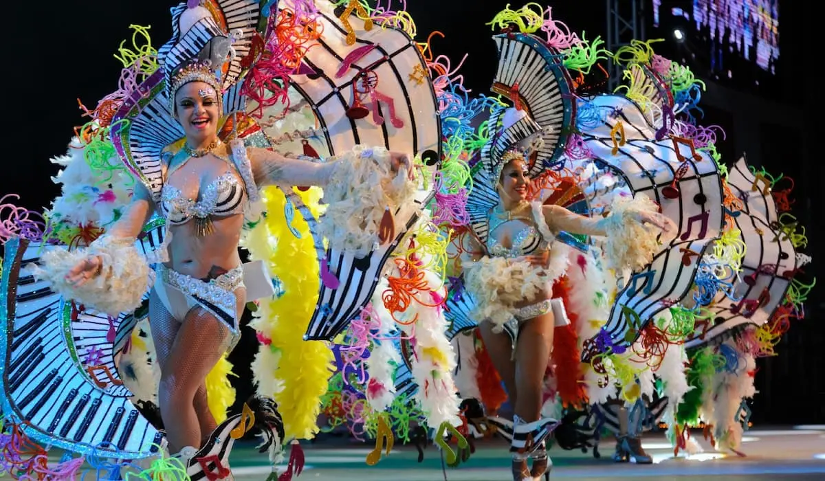 Bailarinas con trajes de carnaval azules y plumas, en escenario con abanicos coloridos